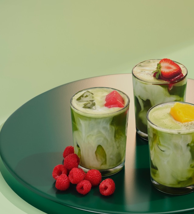 Three glasses filled with matcha placed on a circular tray with raspberries, mango and strawberries on top.