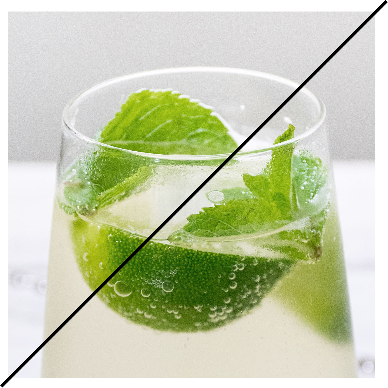 A glass filled with a drink, slice of lime and mint.