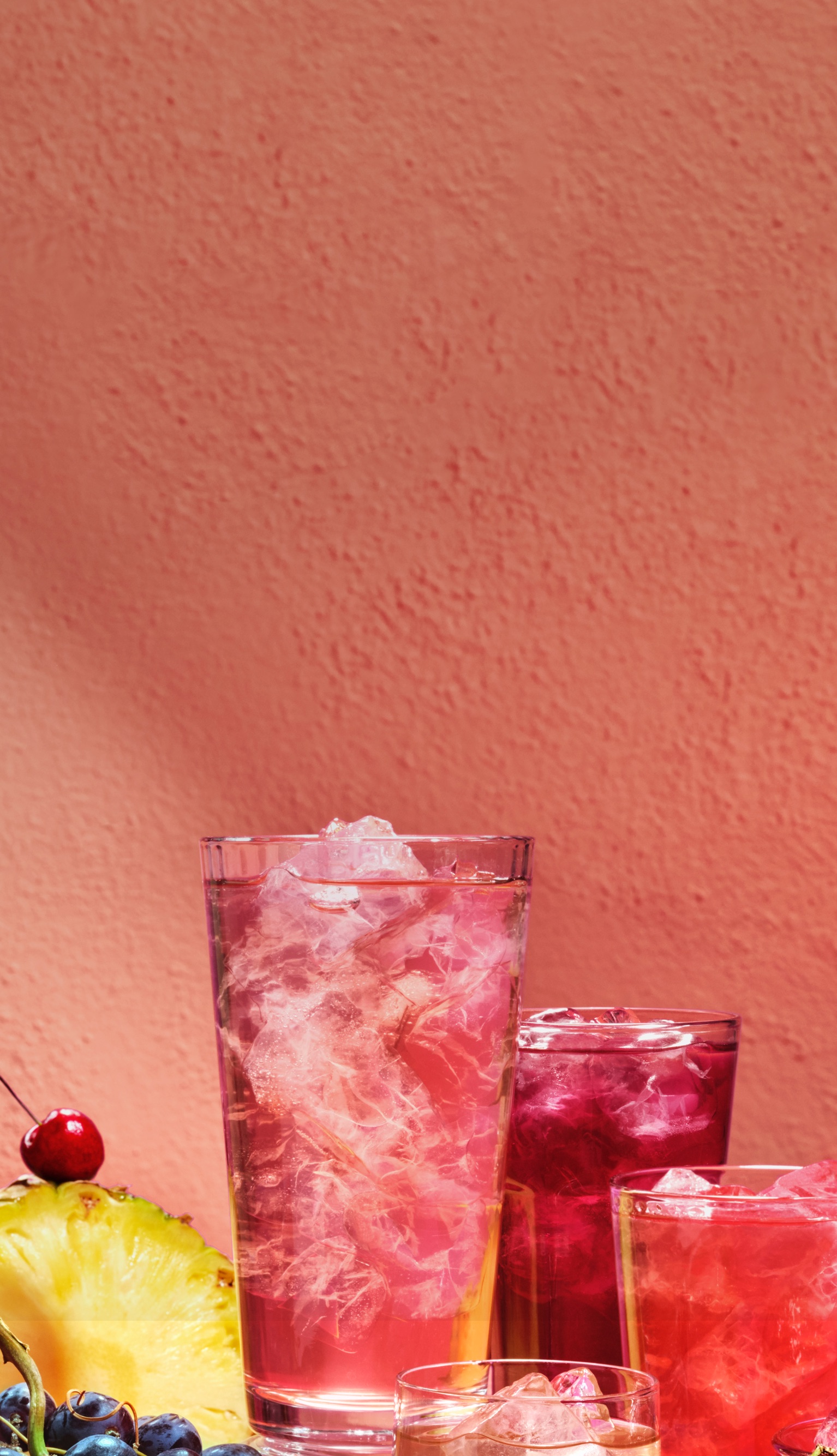 Des verres variés remplis de thés glacés à côté d’une montagne de fruits tropicaux.