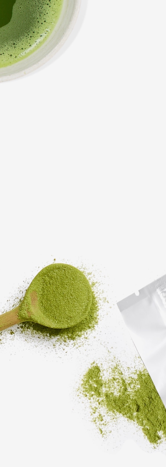 A cup filled with matcha next to a wooden spoon and bag filled with matcha.