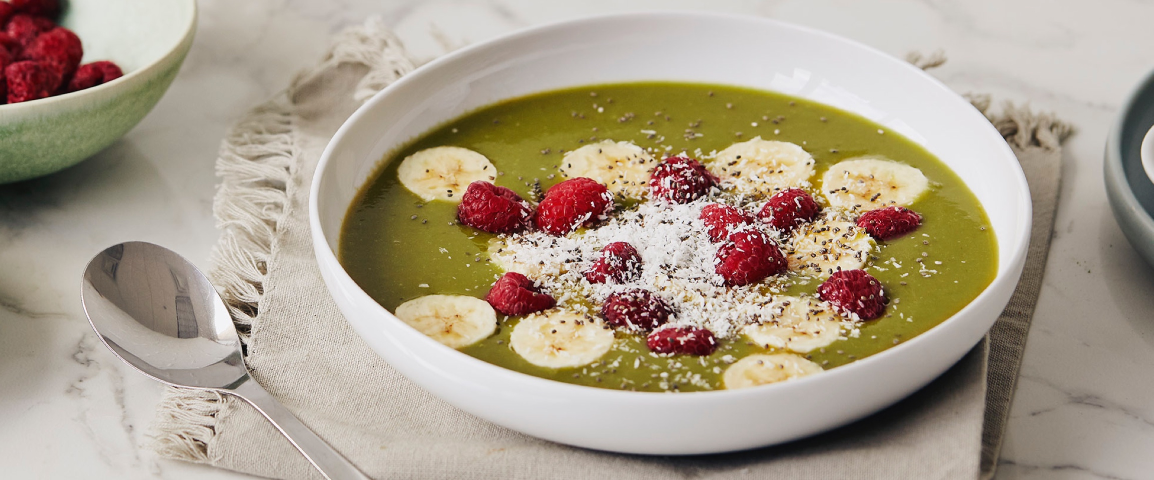 Matcha smoothie in a bowl with bananas and raspberries.