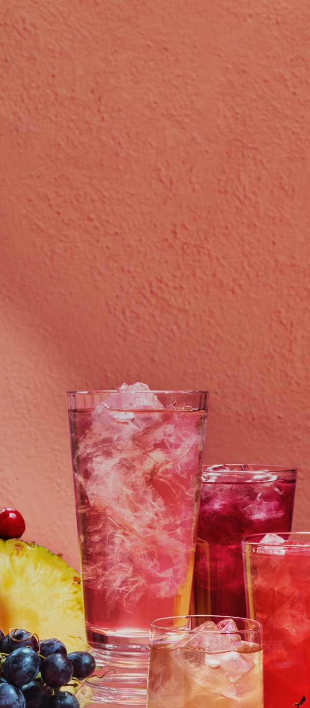 Des verres variés remplis de thés glacés à côté d’une montagne de fruits tropicaux.