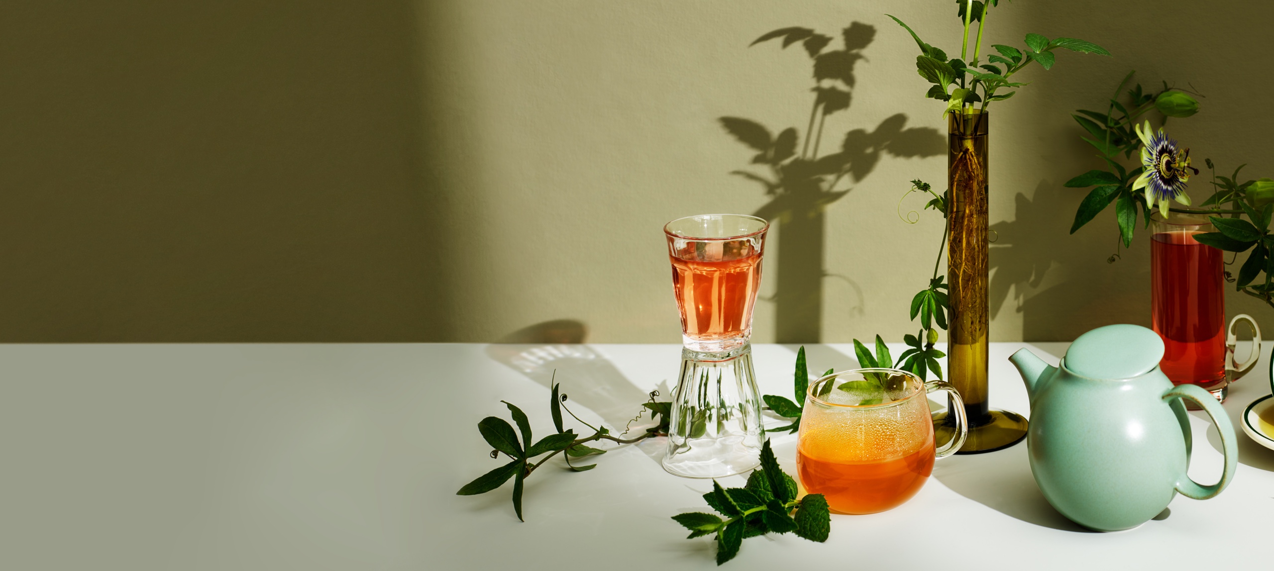 Thés variés dans des verres, placés à côté d’une théière et de plantes. 