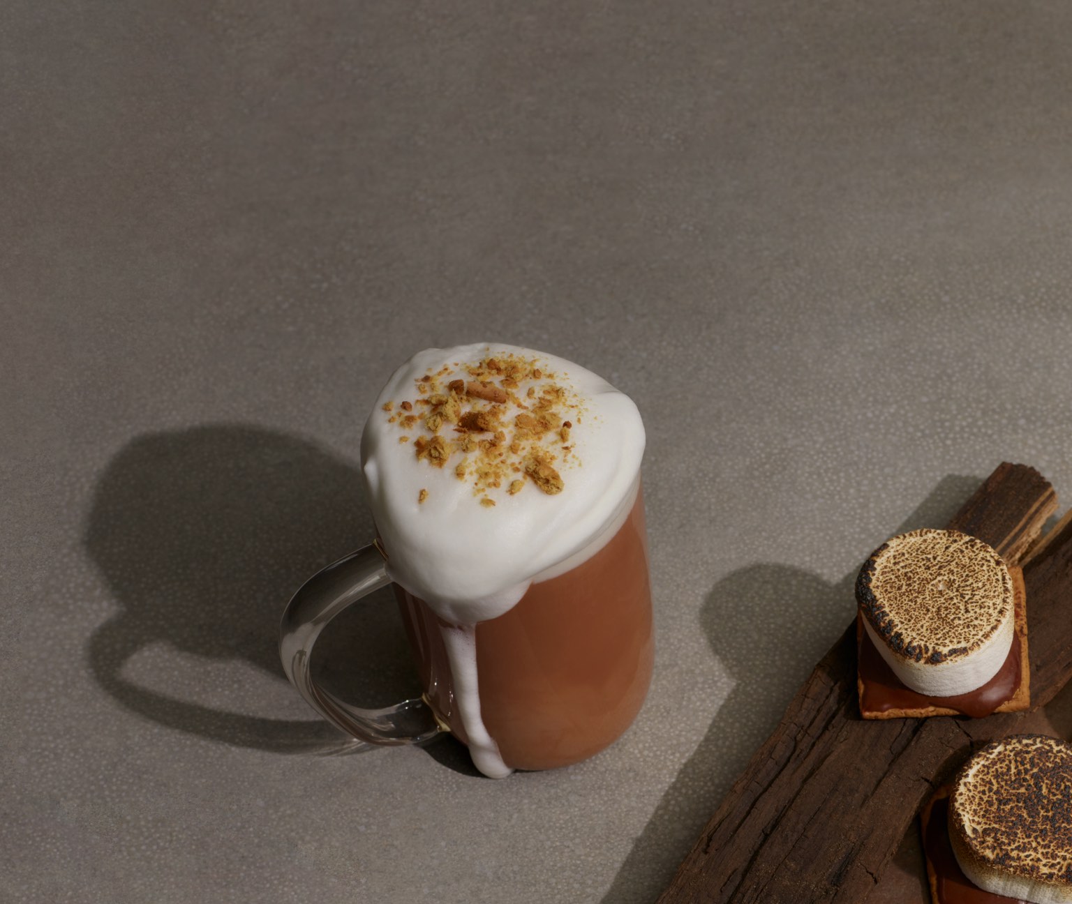 Clear 16 oz glass mug filled with chai latte topped with cinnamon. S’mores dessert with toasted marshmallows.
