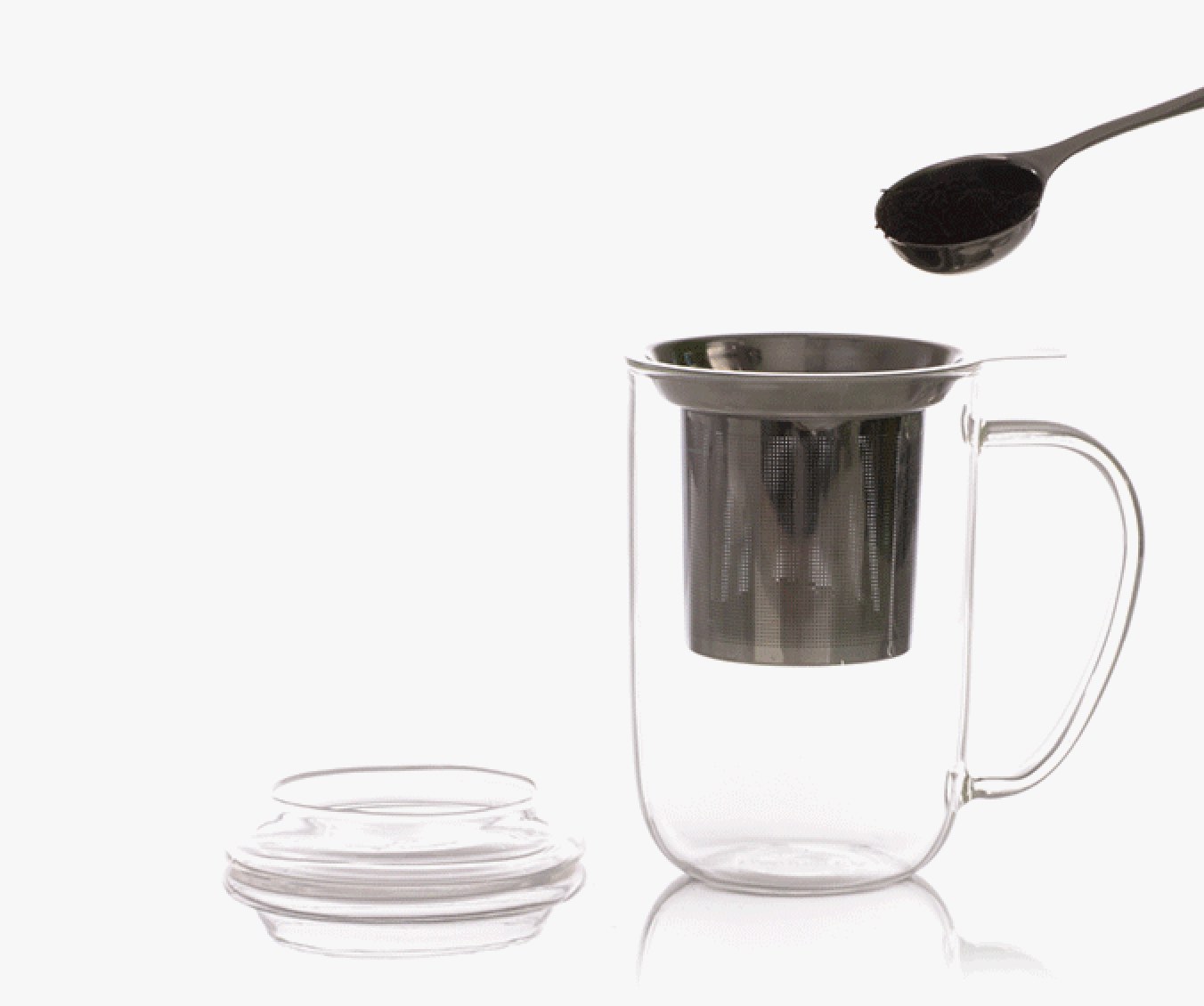 Spoon adding loose leaf tea to stainless steel tea infuser in empty clear 16 oz glass mug.