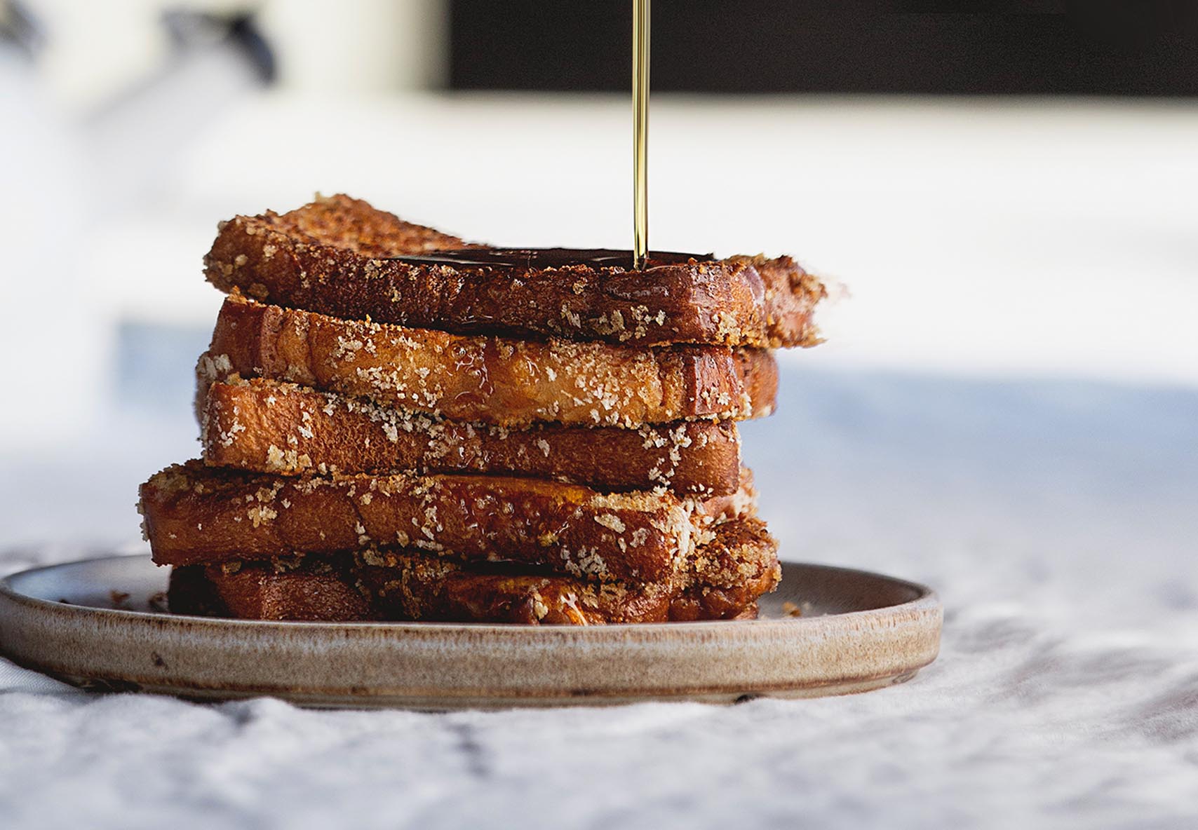 A close up shot of a stack of French toast with maple syrup drizzling on top.